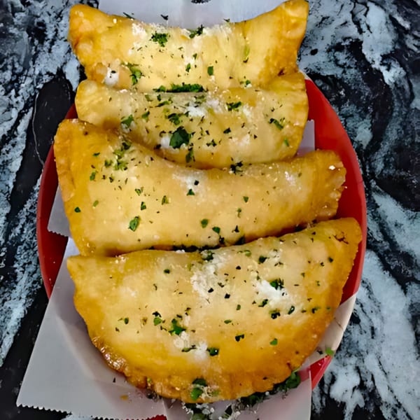 Four golden-brown fried calzones, topped with parsley and parmesan, served on a red plate.