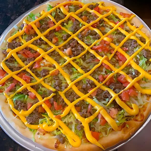 A taco pizza from 2 Brothers Pizzeria, topped with ground beef, lettuce, tomatoes, and a cheese sauce drizzle.