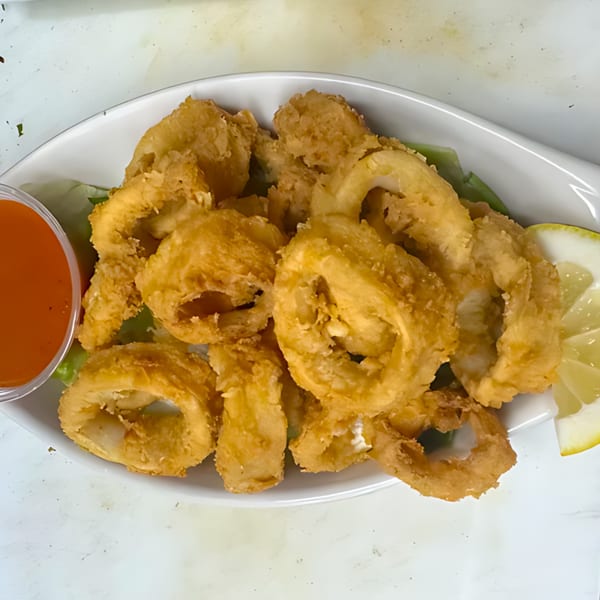 Golden-fried calamari rings on a white plate with a side of red sauce and lemon wedges.
