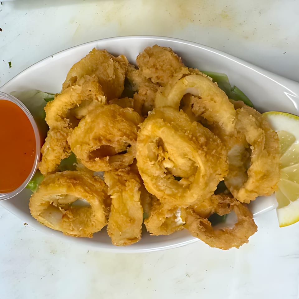 Golden-fried calamari rings on a white plate with a side of red sauce and lemon wedges.
